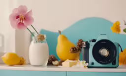 a blue camera sitting next to some fruit and flowers