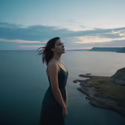 a woman is standing in front of a cliff by the ocean