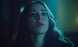 a woman standing in a darkened room looking off into the distance