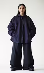the woman stands in a black coat, black jeans and black sneakers