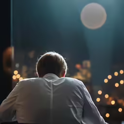 a person in white shirt sitting on chair facing city lights
