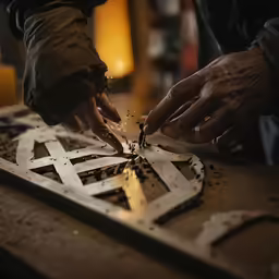 a pair of hands are holding wood as they work on an intricate object