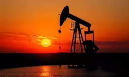 the sun rising above the horizon behind an oil pump