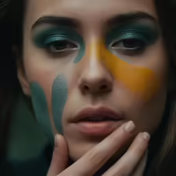 the face of a woman with green, yellow and blue make - up