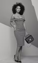 woman with afro hairs in grey dress and heels holding black and white purse