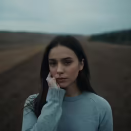 a young girl with brown eyes is standing on a field