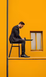man sitting in a chair outside a yellow building looking at his phone
