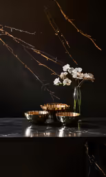 white flowers in a glass vase with gold bowls