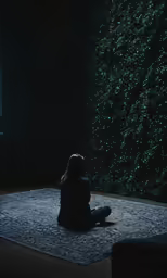 a person kneeling down on a rug in front of some bushes