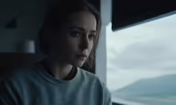 the woman looks outside of a window and looks into the distance