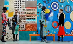 three women in colorful dress standing by an art display