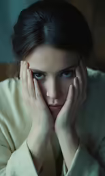 a woman that is looking down and holding her hands to the face