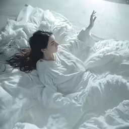 a woman laying on top of a bed covered in white sheets
