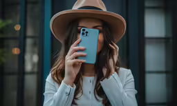 a woman wearing a hat holds her cell phone