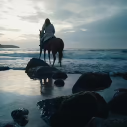 a woman riding on the back of a horse on top of a beach