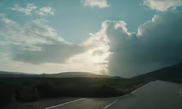 clouds are hovering over a road surrounded by brush and trees