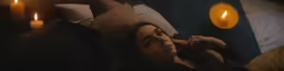 woman on bed staring in the dark with yellow candles lit
