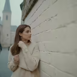a woman leaning up against a brick wall next to a stone building