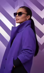 a woman in sunglasses and purple coat posing for the camera