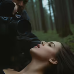 a young woman holding her camera up as she lies down in the woods