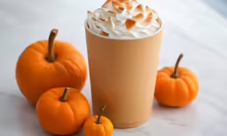a pumpkin drink is on the counter beside five oranges