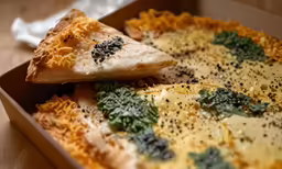 a pizza with cheese, greens, and a slice is displayed in the box