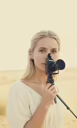 a woman holding a camera up to the side with a tripod in her hand