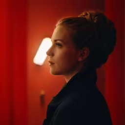 woman with short hair standing in front of the wall with red lighting