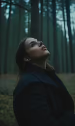 a woman looks upward in the middle of a pine forest