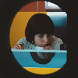 a girl in an office setting looks through a circular hole in a wall