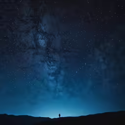 a lone person standing on a mountain with the night sky