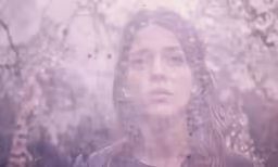 a woman looking out through a window covered with water droplets