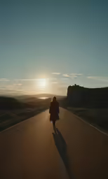 a woman walking across a road with a sunset in the background