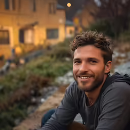 a man in grey shirt sitting next to house