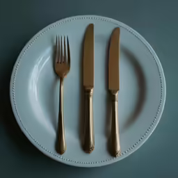 two gold colored forks and a knife on a white plate