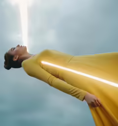 a woman in a yellow costume is holding the arm of a light saber in her hand