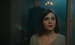 a girl looks at the camera while a man stands behind her