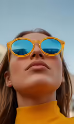 woman wearing bright yellow sunglasses looking up to the sky