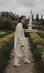 a woman in white clothes stands on a path near a bird statue