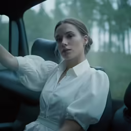 a woman with long hair sitting in a car holding her hand to the side of her head