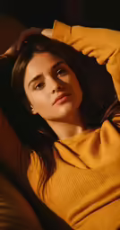 a woman poses in a yellow sweater and a black background