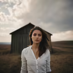 a woman stands outside a small shed in a field