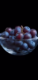 plums in a glass bowl sitting on a black surface