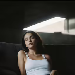 a young woman sitting on a couch with a tank top on