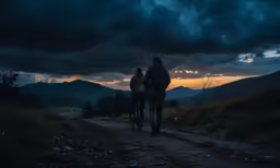 two people walking down a dirt road near a forest