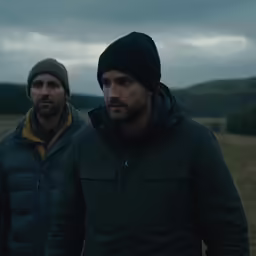 two men standing outside, wearing hats and winter clothes