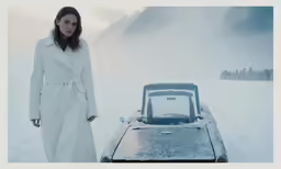 a woman in long coat posing next to vehicle with snow