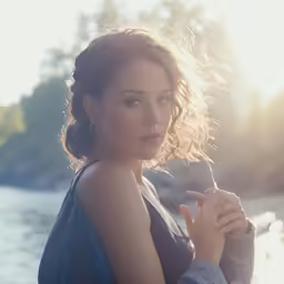 a woman is sitting by a water with her hands clasped around the neck
