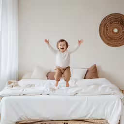 a toddler jumping on a bed with white sheets
