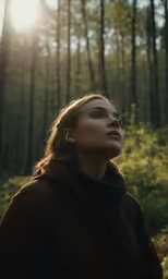 a woman standing in a forest gazing up at the sunlight